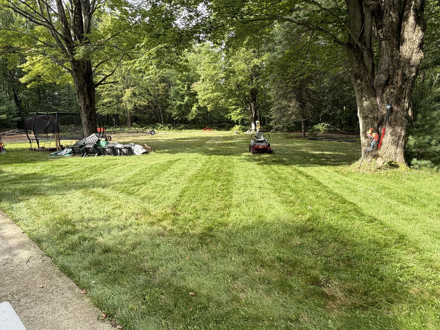 Freshly mowed lawn with clean stripe pattern and a zero-turn mower parked at the edge of the yard