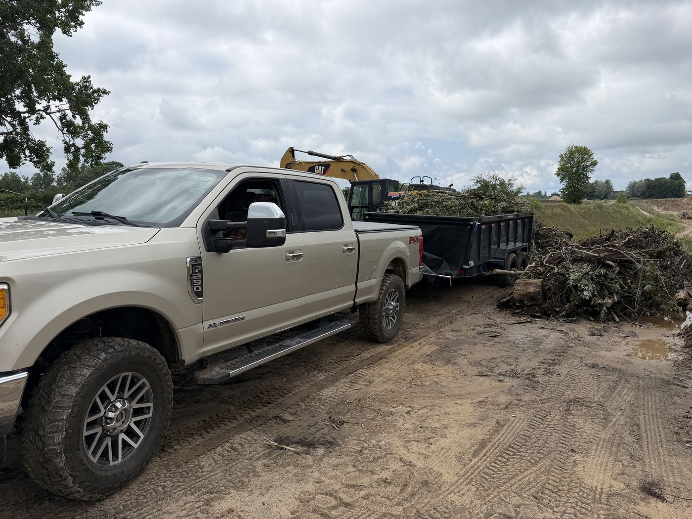 Truck and trailer loaded with cleared brush next to an excavator during a land-clearing job